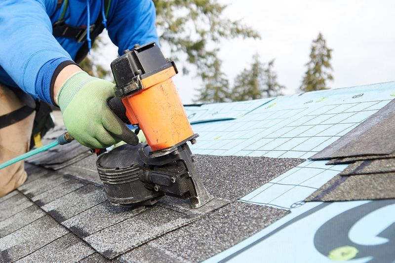 Roofer fixing shingles with a nail gun